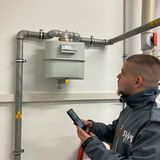 Ein Zählerableser der Stadtwerke Stralsund prüft aufmerksam einen Gaszähler und hält ein mobiles Erfassungsgerät in der Hand in einem technischen Raum.