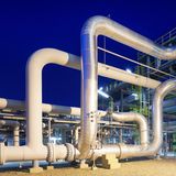 Komplexe industrielle Rohrleitungen vor einer Chemiefabrik bei Nacht, beleuchtet durch zahlreiche Lichter, die die technische Komplexität und moderne Infrastruktur betonen