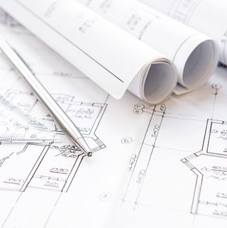 Entwurfsskizzen und technische Zeichnungen verteilt auf einem Arbeitstisch, wobei Bleistifte und ein Zirkel die intensive Planungsphase eines Architektur- oder Ingenieurprojekts andeuten.